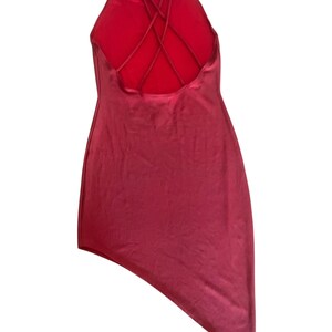 May include: A solid red mini dress featuring a high neckline and a strappy back design with multiple thin crisscrossing straps. The garment has a smooth, satin-like finish and an asymmetrical hemline that is longer on the right side.