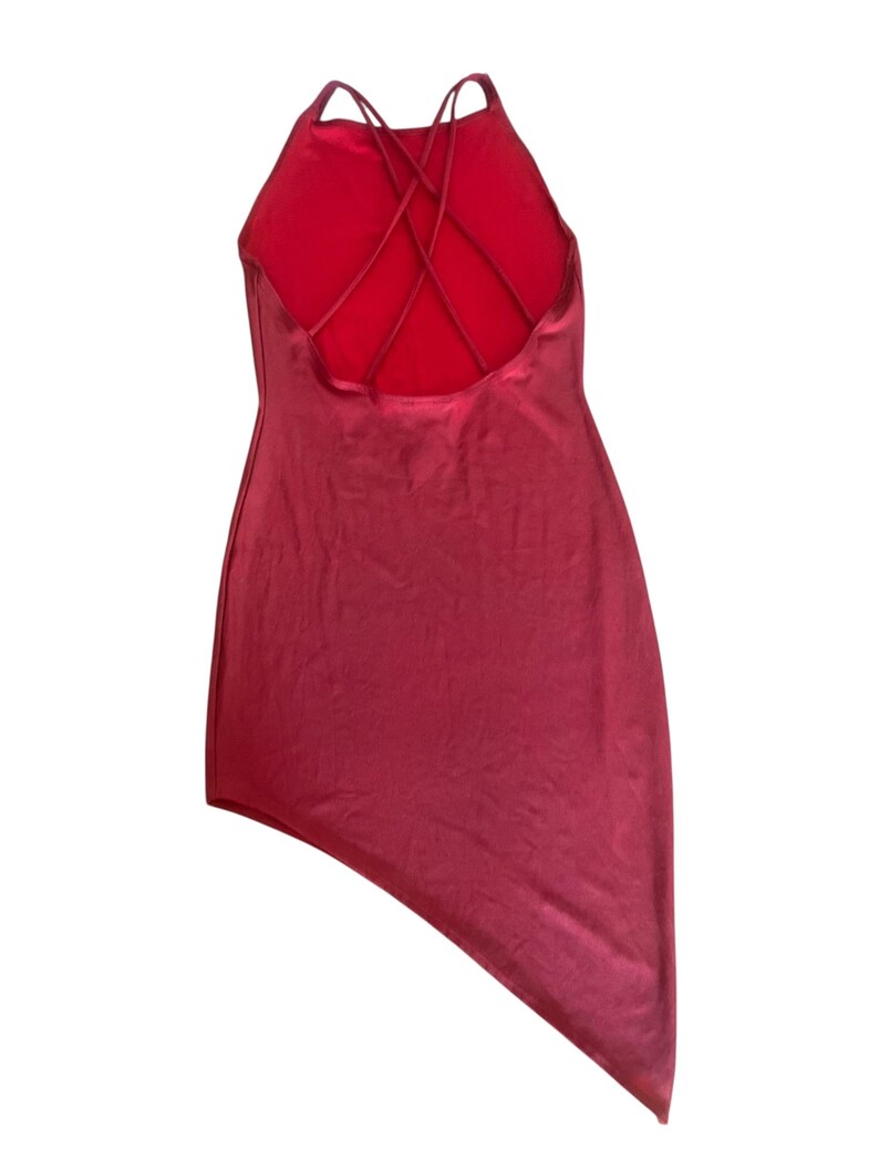May include: A solid red mini dress featuring a high neckline and a strappy back design with multiple thin crisscrossing straps. The garment has a smooth, satin-like finish and an asymmetrical hemline that is longer on the right side.