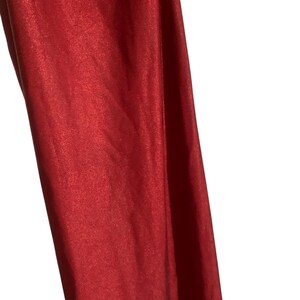 May include: A piece of fabric with a vibrant red color and a distinct metallic, shimmering finish. The material displays a smooth, reflective surface that catches the light, creating subtle variations in tone across the folds and vertical drapes.