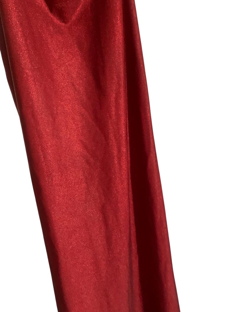 May include: A piece of fabric with a vibrant red color and a distinct metallic, shimmering finish. The material displays a smooth, reflective surface that catches the light, creating subtle variations in tone across the folds and vertical drapes.