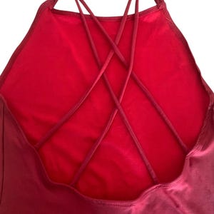 May include: A solid red garment featuring a high neckline and a back design composed of multiple thin, crisscrossing straps that form an intricate web pattern. The fabric appears smooth and uniform in color, with visible stitching along the edges.