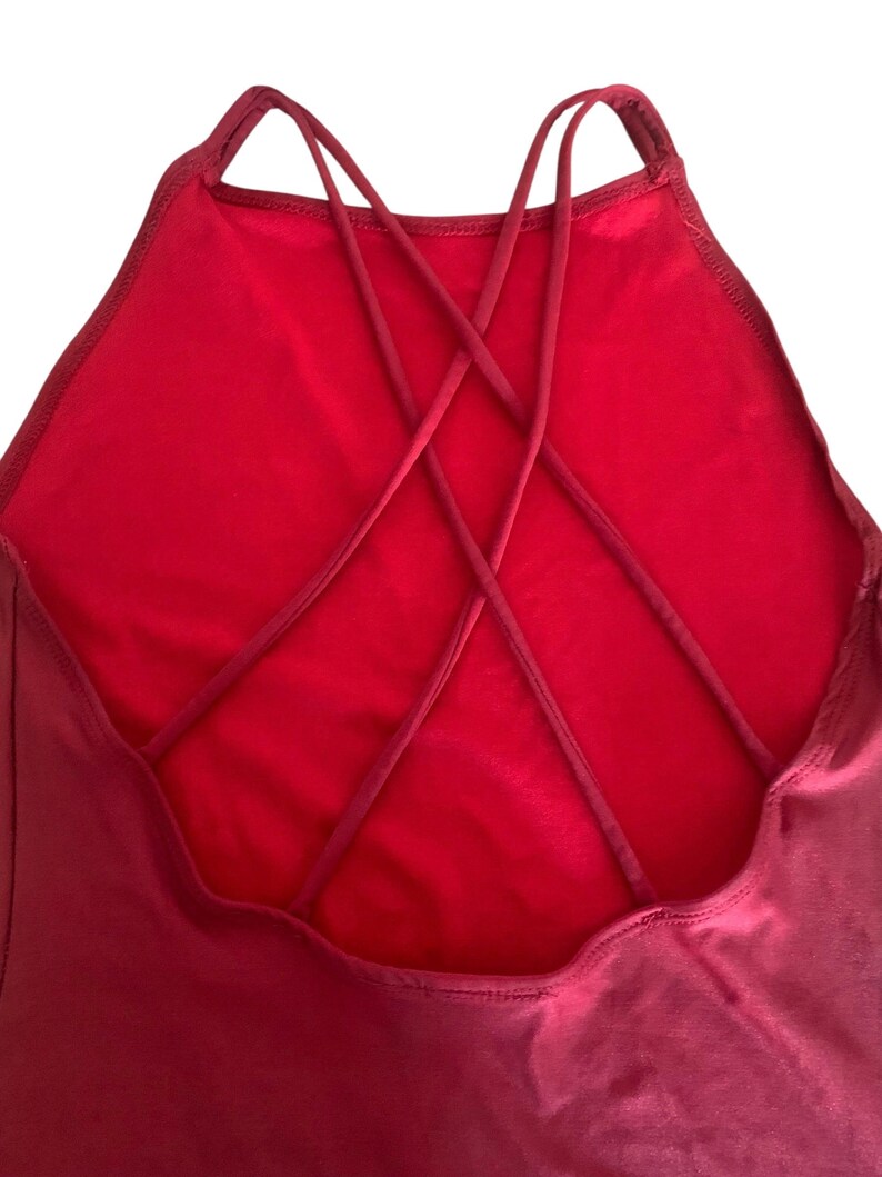 May include: A solid red garment featuring a high neckline and a back design composed of multiple thin, crisscrossing straps that form an intricate web pattern. The fabric appears smooth and uniform in color, with visible stitching along the edges.