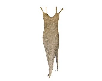 May include: A sleeveless, mid-length dress in a champagne gold hue, fully covered in intricate, shimmering beadwork. The garment features a V-neckline, thin shoulder straps, and a distinct side slit that extends from the hemline upward.