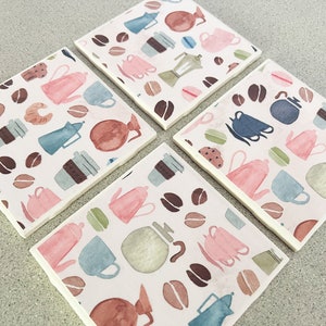 May include: Set of four square ceramic coasters with a white background and a repeating pattern of coffee cups, coffee beans, and coffee pots in shades of pink, blue, green, and brown.