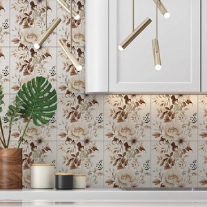 Puede incluir: Un salpicadero de cocina con azulejos blancos que presentan un patr&oacute;n floral en tonos marrones y beige. Una planta en maceta con hojas verdes se encuentra en la encimera frente al salpicadero.