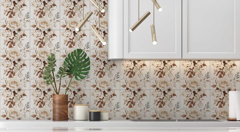 Puede incluir: Un salpicadero de cocina con azulejos blancos que presentan un patr&oacute;n floral en tonos marrones y beige. Una planta en maceta con hojas verdes se encuentra en la encimera frente al salpicadero.