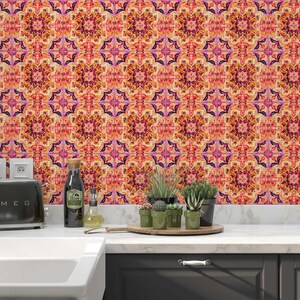 May include: A kitchen with a patterned orange, pink, and purple backsplash. A black toaster, sink, and a wooden tray with small potted plants sit on the countertop. A stainless steel tap and extractor fan are also visible.