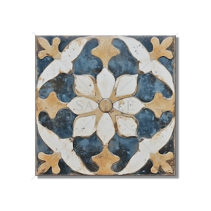 May include: Square decorative tile with a floral design. The tile features a central white flower with blue and tan accents. The background is a distressed blue, and the edges are a darker blue.