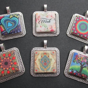 May include: Six square pendants with silver-colored frames. Each pendant features a unique design: a heart, floral pattern with the word "Wish", a mandala, a geometric pattern, a Hamsa hand, and a colorful tree.