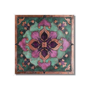 May include: A square tile with a copper-colored frame and a green, pink, and purple floral design. The design features a central flower with four petals and intricate patterns around it.