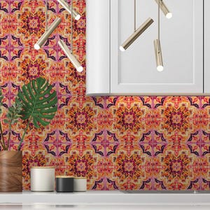 May include: A kitchen backsplash featuring a repeating floral pattern in orange, pink, and purple hues. The design resembles a mandala. A wooden vase with green leaves and a white countertop are in the foreground.