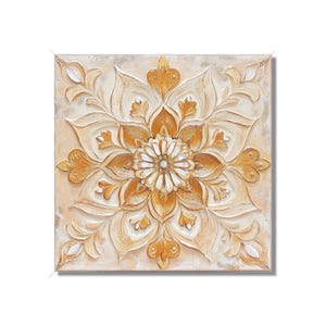 May include: A square canvas painting with a raised, textured design of a white flower with gold accents. The flower is surrounded by a symmetrical pattern of gold leaves and swirls.