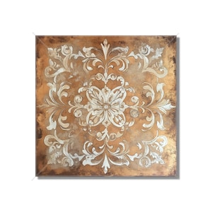 May include: Square wall art with a distressed copper-colored background and a white floral design. The design is symmetrical, with a central flower and swirling patterns extending to the edges. The artwork has a vintage, antique aesthetic.