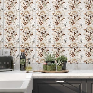 Puede incluir: Una cocina con un salpicadero de azulejos blancos con un patr&oacute;n floral. El salpicadero est&aacute; sobre una encimera blanca con un fregadero de acero inoxidable, una tostadora negra y una variedad de plantas en macetas. La encimera tambi&eacute;n est&aacute; sobre gabinetes gris oscuro.