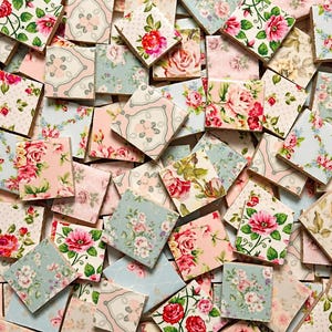 May include: A collection of square wooden tiles featuring a variety of floral patterns in shades of pink, green, blue, and cream. Each tile displays distinct botanical illustrations, including roses and small blossoms, with some tiles showing polka dots.