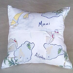 May include: White pillow with a blue and yellow design featuring sailboats and palm trees. The pillow has the words "Maui" and "Aloha" printed on it.