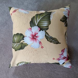 May include: A yellow throw pillow with a tropical print featuring white hibiscus flowers and green leaves.
