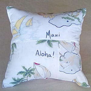May include: White pillow with a blue and yellow island scene and the words "Maui Aloha!" embroidered on it.