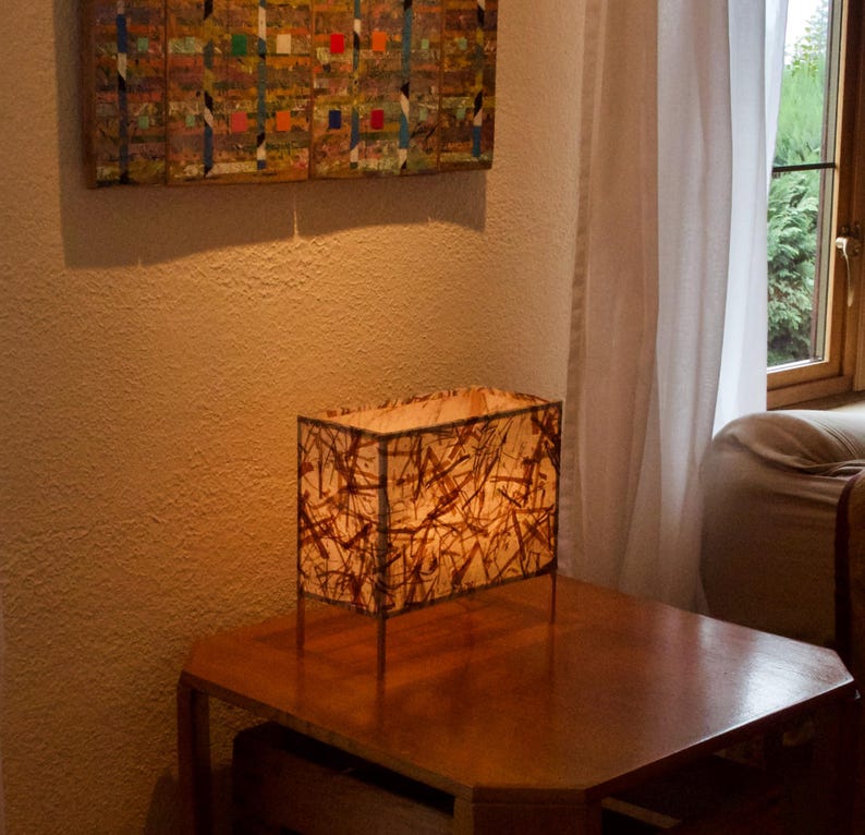 Pode incluir: Um abajur de mesa retangular com um abajur estampado em marrom e branco. A l&acirc;mpada est&aacute; em uma mesa de madeira.