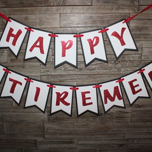 May include: A banner with the words "HAPPY RETIREMENT" in red glitter letters on white pennants with black borders. The pennants are strung on a red ribbon against a wooden background.