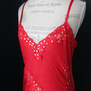 May include: A red slip dress with silver accents and lace detailing. The dress has a V-neckline and is sleeveless. The dress is on a mannequin.