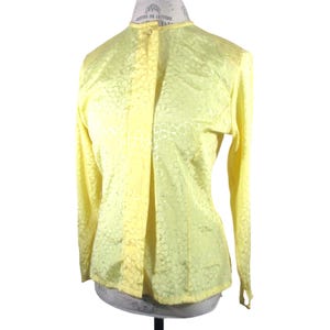 May include: A yellow blouse with a floral pattern. The blouse has a button-up front and long sleeves.
