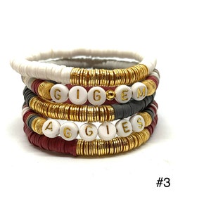 May include: A set of five bracelets with white beads and gold accents. The bracelets spell out the words "GIG'EM" and "AGGIES".