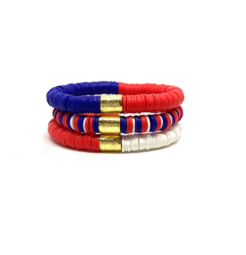 May include: Three stacked bracelets featuring red, white and blue beads with gold accents. The bracelets are made from plastic and are ideal for adding a touch of colour to any outfit.
