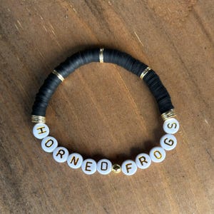 May include: Black beaded bracelet with gold accents and white beads spelling "Horned Frogs".