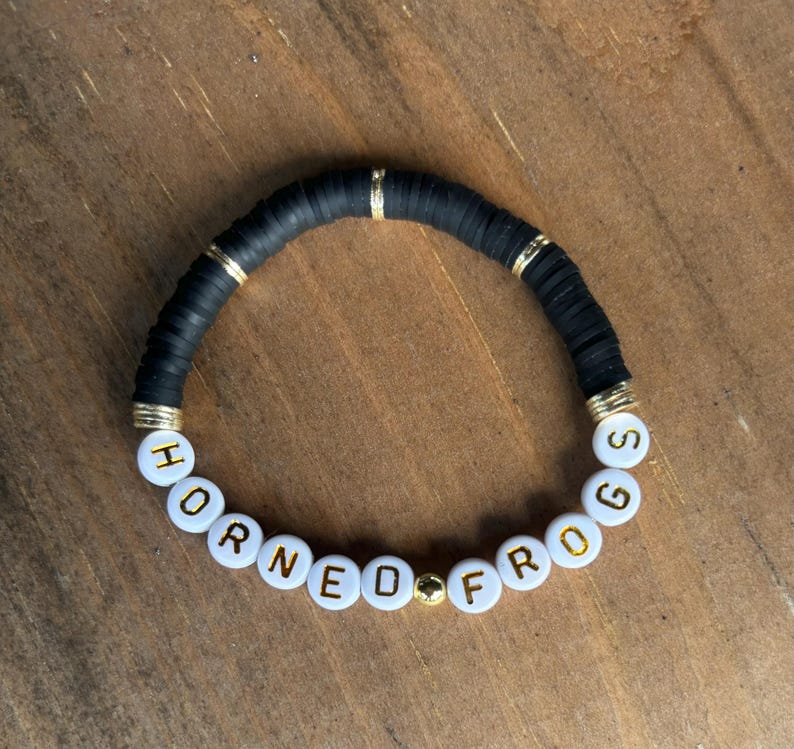 May include: Black beaded bracelet with gold accents and white beads spelling "Horned Frogs".