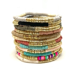 May include: A stack of colorful beaded bracelets with gold accents. The bracelets are made of various colors, including white, black, gray, pink, red, blue, and green.
