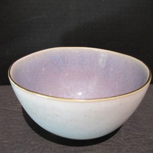 May include: A ceramic bowl with a pale blue exterior and a lavender interior. The rim has a thin gold-coloured band. The bowl is round and has a smooth surface. It is likely used for serving food or as a decorative item.