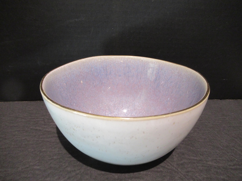 May include: A ceramic bowl with a pale blue exterior and a lavender interior. The rim has a thin gold-coloured band. The bowl is round and has a smooth surface. It is likely used for serving food or as a decorative item.