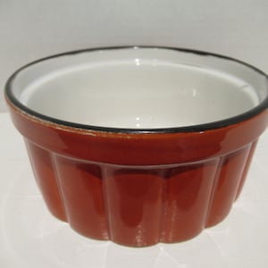 May include: A small, orange ceramic ramekin with a white interior and a black rim. The ramekin has a fluted design around the sides.