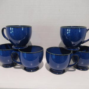 May include: Six blue ceramic teacups with a speckled glaze. The cups are stacked in a pyramid shape.