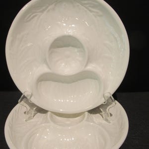 May include: Two-tiered white ceramic serving dish with a leaf pattern. The top tier has three sections, including a central circular dip bowl. The bottom tier is a matching plate. Clear plastic supports hold the top tier.