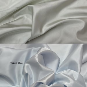 Puede incluir: Se muestran dos secciones de tela. La secci&oacute;n superior es de color plata clara, y la secci&oacute;n inferior es azul congelado. La tela tiene una textura brillante, similar al sat&eacute;n, con pliegues y arrugas visibles.