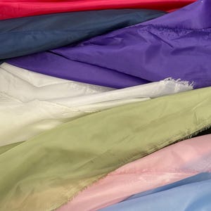 May include: A close-up of layered fabric in various colors. The colors include hot pink, navy blue, purple, white, light green, pink, and light blue. The fabric appears to be a lightweight, possibly synthetic material.