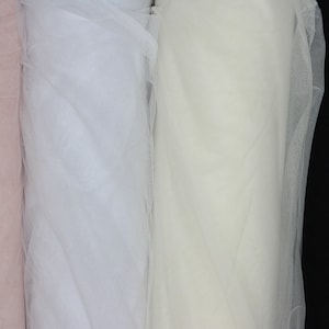 May include: Three rolls of tulle fabric in pink, white, and ivory colors. The fabric is sheer and delicate, perfect for crafting and sewing projects.