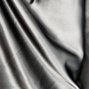 May include: A close-up of a smooth, black fabric with a soft, silky texture. The fabric is draped and folded, creating a luxurious and elegant look.