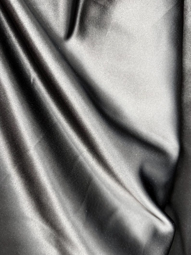 May include: A close-up of a smooth, black fabric with a soft, silky texture. The fabric is draped and folded, creating a luxurious and elegant look.