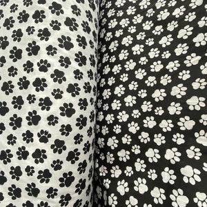 May include: Two rolls of fabric with a paw print pattern. One roll has black paw prints on a white background, and the other roll has white paw prints on a black background.