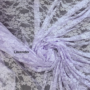 May include: A lavender-colored lace fabric featuring a delicate white floral pattern throughout the material. The fabric is gathered in the center, creating soft folds and drapes that highlight the intricate, repeating botanical lace design.