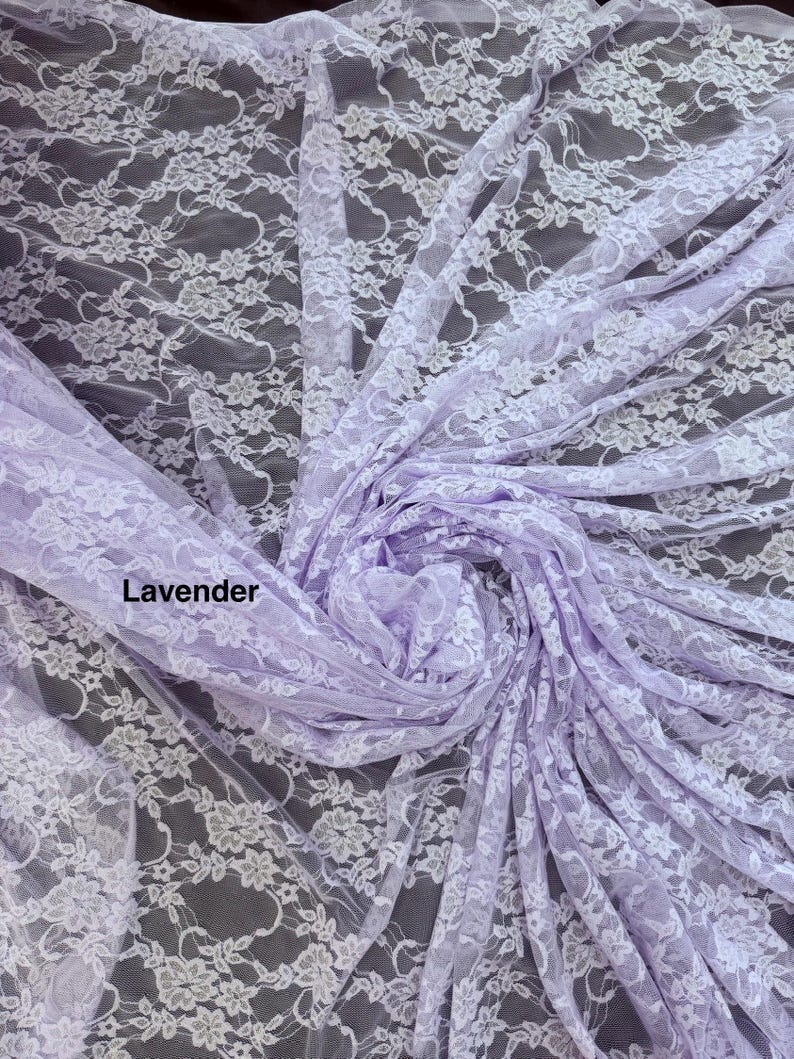 May include: A lavender-colored lace fabric featuring a delicate white floral pattern throughout the material. The fabric is gathered in the center, creating soft folds and drapes that highlight the intricate, repeating botanical lace design.