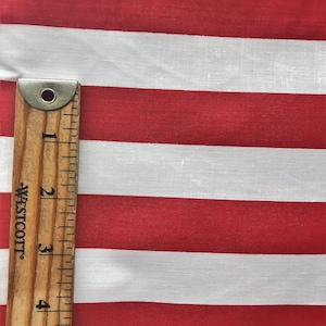 May include: Red and white striped fabric with a wooden ruler measuring 5 inches. The fabric is a cotton blend and has a subtle texture.