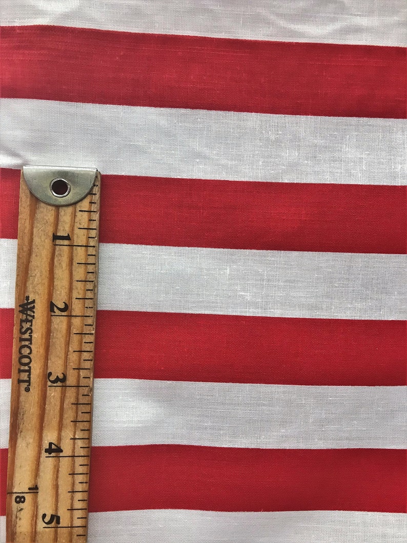May include: Red and white striped fabric with a wooden ruler measuring 5 inches. The fabric is a cotton blend and has a subtle texture.