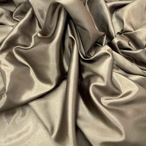 Puede incluir: Tela color chocolate con un brillo lustroso, drapeada en suaves pliegues. La tela tiene una textura suave y un brillo sutil, creando una apariencia lujosa. La palabra "Chocolate" est&aacute; impresa en la tela.