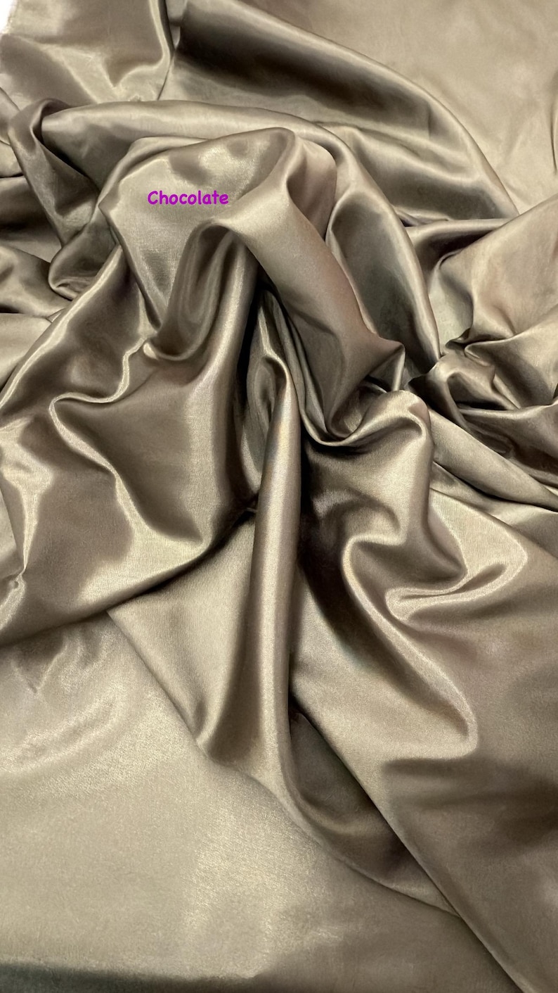 Puede incluir: Tela color chocolate con un brillo lustroso, drapeada en suaves pliegues. La tela tiene una textura suave y un brillo sutil, creando una apariencia lujosa. La palabra "Chocolate" est&aacute; impresa en la tela.