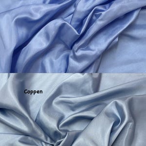 Puede incluir: Dos secciones de tela azul claro con un brillo sedoso. La secci&oacute;n superior est&aacute; etiquetada como "Corn blue", y la secci&oacute;n inferior como "Coppen". La tela est&aacute; drapeada, creando pliegues y sombras suaves, resaltando su textura y color.