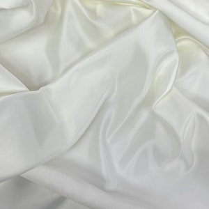 May include: White satin fabric with soft, flowing folds. The fabric is smooth and luxurious, with a subtle sheen.
